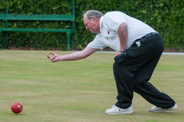 A man kneeling down, just after bowling on an outdoor bowling green